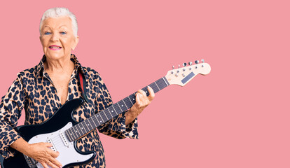 Senior beautiful woman with blue eyes and grey hair with modern look playing electric guitar looking positive and happy standing and smiling with a confident smile showing teeth