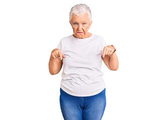 Senior beautiful woman with blue eyes and grey hair wearing casual white tshirt pointing down looking sad and upset, indicating direction with fingers, unhappy and depressed.