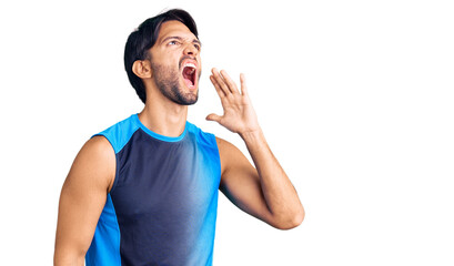 Handsome hispanic man wearing sportswear shouting and screaming loud to side with hand on mouth. communication concept.