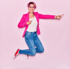 Young beautiful businesswoman with pink short hair wearing  elegant clothes and glasses smiling happy. Jumping with smile on face pointing to the side with fingers over isolated background