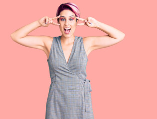 Young beautiful woman with pink hair wearing casual clothes doing peace symbol with fingers over face, smiling cheerful showing victory