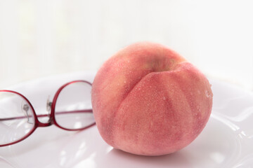 夏の果物白い皿にもられた一個の冷えた桃と女性用メガネ
