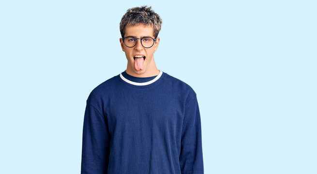 Young handsome man wearing casual clothes and glasses sticking tongue out happy with funny expression. emotion concept.