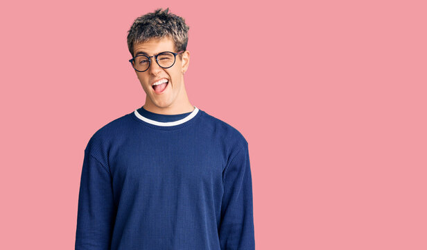 Young handsome man wearing casual clothes and glasses winking looking at the camera with sexy expression, cheerful and happy face.