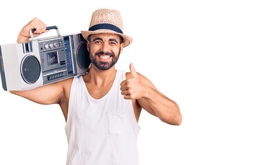 Young hispanic man holding boombox, listening to music smiling happy and positive, thumb up doing excellent and approval sign