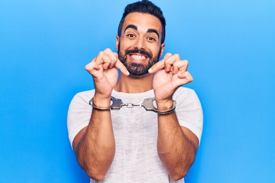Young hispanic man wearing prisoner handcuffs smiling happy pointing with hand and finger