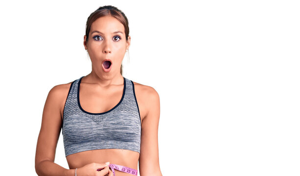 Young beautiful hispanic woman wearing sportswear using tape measure scared and amazed with open mouth for surprise, disbelief face