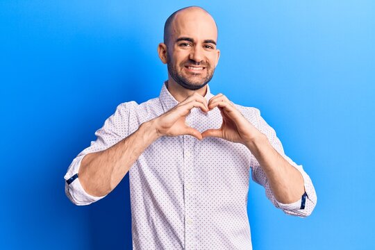 Young handsome bald man wearing elegant shirt smiling in love doing heart symbol shape with hands. romantic concept.