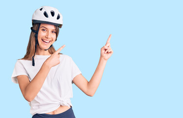 Young beautiful girl wearing bike helmet smiling and looking at the camera pointing with two hands and fingers to the side.
