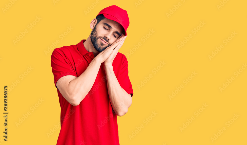 Wall mural young handsome man with beard wearing delivery uniform sleeping tired dreaming and posing with hands