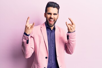 Young handsome man with beard wearing elegant jacket shouting with crazy expression doing rock symbol with hands up. music star. heavy concept.