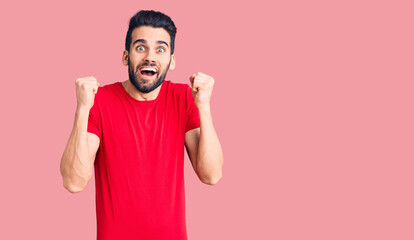 Young handsome man with beard wearing casual t-shirt celebrating surprised and amazed for success with arms raised and open eyes. winner concept.