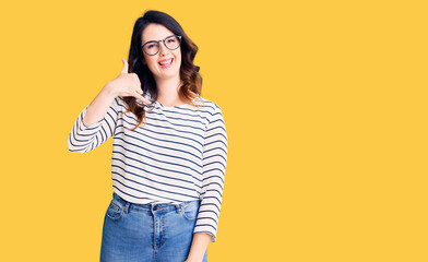 Beautiful young brunette woman wearing casual clothes and glasses smiling doing phone gesture with hand and fingers like talking on the telephone. communicating concepts.