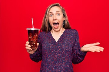 Young beautiful blonde woman drinking a fresh glass of soda celebrating achievement with happy smile and winner expression with raised hand