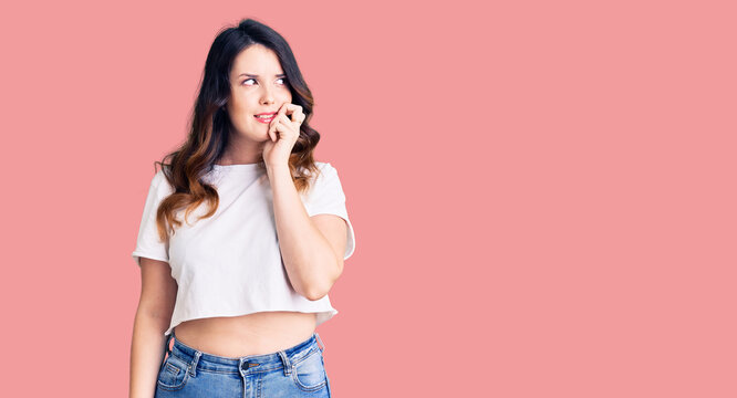 Beautiful young brunette woman wearing casual clothes looking stressed and nervous with hands on mouth biting nails. anxiety problem.