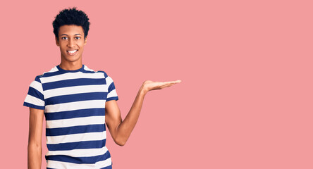 Young african american man wearing casual clothes smiling cheerful presenting and pointing with palm of hand looking at the camera.