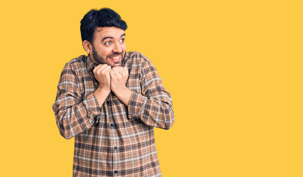 Young hispanic man wearing casual clothes laughing nervous and excited with hands on chin looking to the side