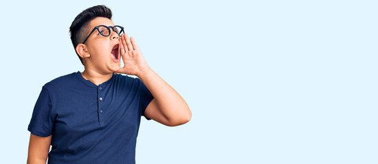 Naklejka premium Little boy kid wearing casual clothes and glasses shouting and screaming loud to side with hand on mouth. communication concept.