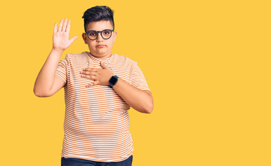 Little boy kid wearing casual clothes and glasses swearing with hand on chest and open palm, making...