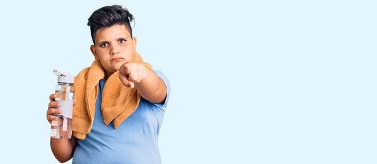 Little boy kid wearing sportswear drinking bottle of water pointing with finger to the camera and to you, confident gesture looking serious