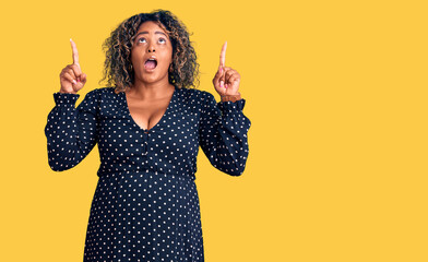 Young african american plus size woman wearing casual clothes amazed and surprised looking up and pointing with fingers and raised arms.