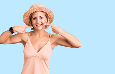 Young blonde woman wearing summer hat smiling cheerful showing and pointing with fingers teeth and mouth. dental health concept.