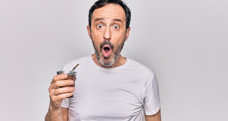 Middle age handsome man drinking cup of mate tea over isolated white background scared and amazed with open mouth for surprise, disbelief face