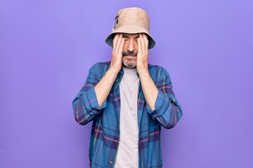 Middle age handsome man wearing casual shirt and hat over isolated purple background with hand on head, headache because stress. Suffering migraine.