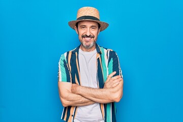 Middle age handsome tourist man on vacation wearing shirt and hat over blue background happy face...