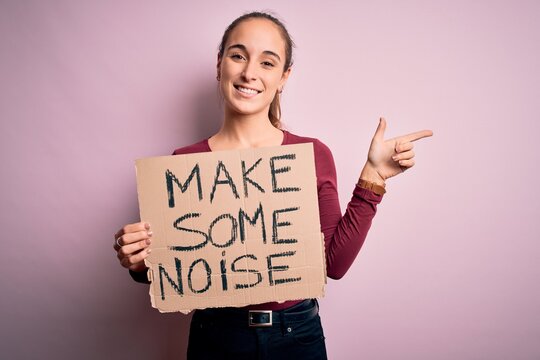 Beautiful activist woman holding banner with make some noise message over pink background very happy pointing with hand and finger to the side