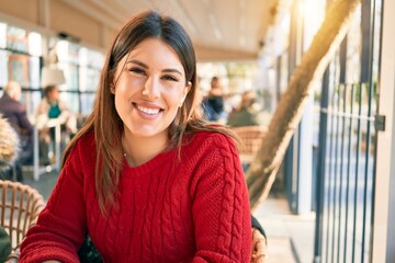 Young beautiful brunette woman smiling happy and confident. Sitting with smile on face relaxing at restaurant