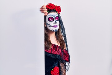 Young woman wearing day of the dead custome holding blank empty banner looking away to side with smile on face, natural expression. laughing confident.