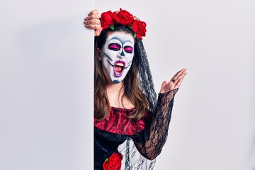 Young woman wearing day of the dead custome holding blank empty banner crazy and mad shouting and yelling with aggressive expression and arms raised. frustration concept.