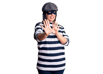 Young beautiful brunette woman wearing burglar mask disgusted expression, displeased and fearful...