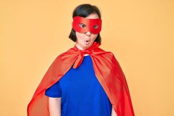 Brunette woman with down syndrome wearing super hero costume scared and amazed with open mouth for surprise, disbelief face