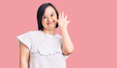 Brunette woman with down syndrome wearing casual white tshirt waiving saying hello happy and smiling, friendly welcome gesture © Krakenimages.com