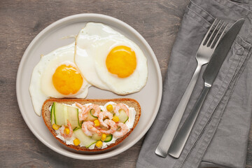 Sandwich with cheese, cucumber and shrimp, fried eggs on a plate and coffee on the table. Healthy breakfast. Top View