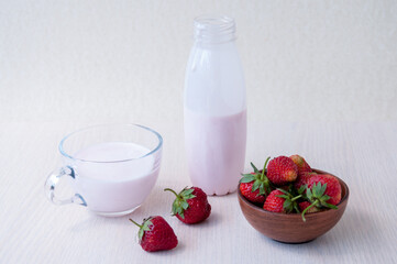 Red strawberries in a clay Cup and yogurt in a bottle and glass mug on the table