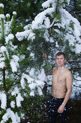 young man in a winter forest sprinkles snow to harden the body