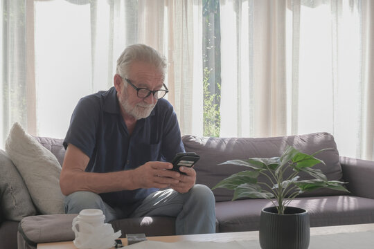 Caucasian old man living alone lifestyle; using smartphone, cigarette and coffee cup put on the table in cozy living room and sunny day.