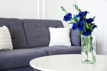 A bouquet of blue flowers in a glass vase on a round table next to a blue sofa