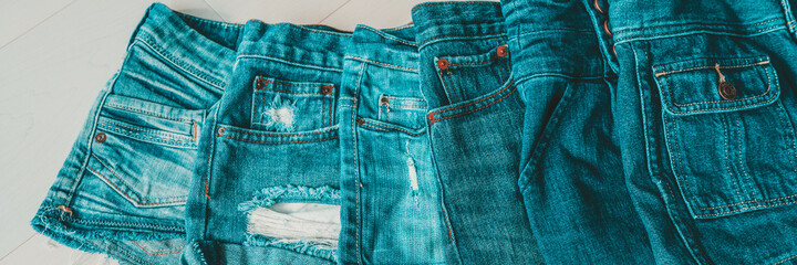 Jeans shorts layered by shades of blue indigo dye. Different styles of distressed denim fashion textile fabric banner panoramic.