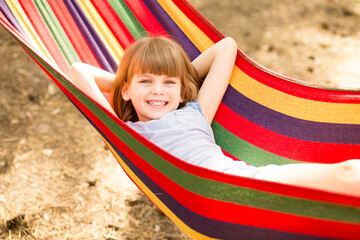 Happy lovely child girl relaxing in colorful hammock in summer forest.