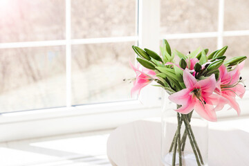 Bouquet of artificial flowers in a glass vase on a white table in front of a large window