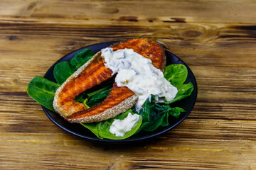Grilled salmon steak with spinach and tartare sauce on wooden table