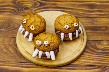 Halloween dessert: Toothed monsters made of oatmeal cookies, chocolate spread and marshmallows on a wooden table