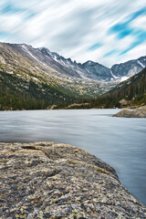 Fototapeta na wymiar Mills lake long exposure. Rocky mountain national park lake in colorado. Blue water and snow capped mountains visible. Pines, rocks, and water lead through the scene.
