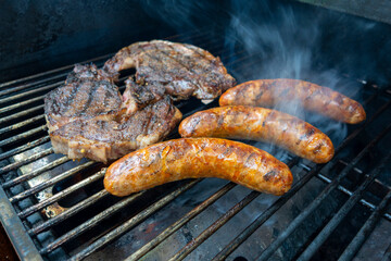 steaks and sausage cooking and smoking food on an outdoor grill