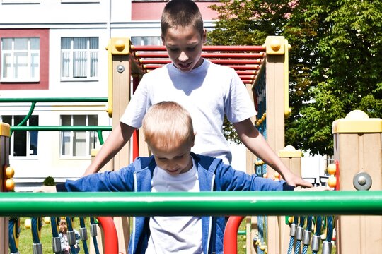 Children play in the open area. Two brothers play in school or kindergarten. Active childs on a colorful slide and swing. Healthy summer activities for children. Summer active sport leisure for kids.