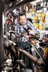 Happy man considers bicycle handlebar in store when choosing bike
